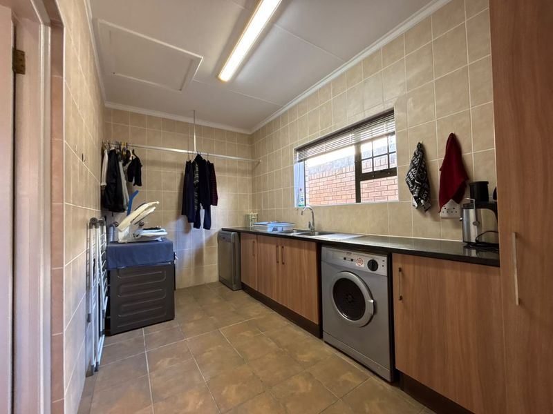 A functional laundry room featuring tiled walls and floors, built-in wooden cabinetry, a stainless steel sink, and space for under-counter appliances.