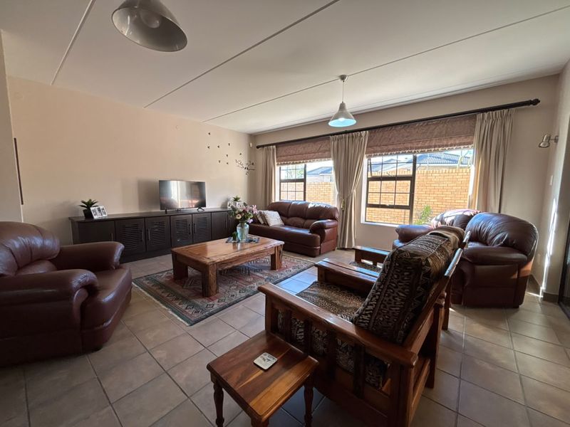 A spacious living room featuring tiled flooring, large windows with curtain rails, and neutral wall tones, offering a comfortable and functional family living space.