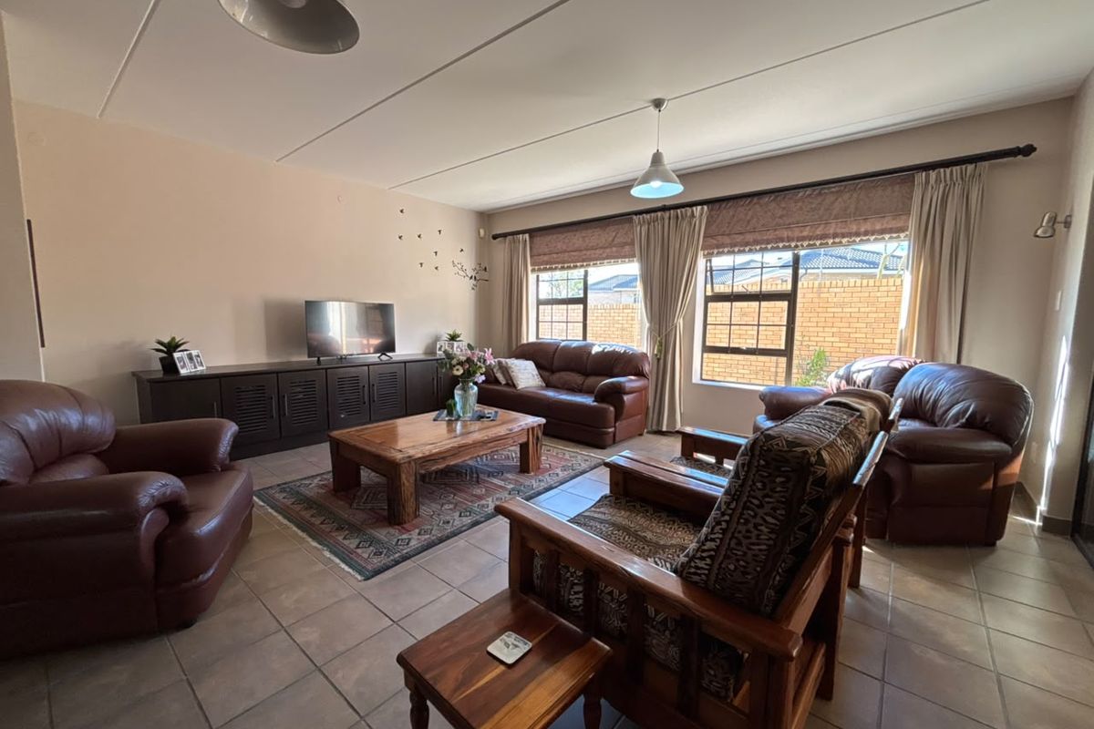 A spacious living room featuring tiled flooring, large windows with curtain rails, and neutral wall tones, offering a comfortable and functional family living space.