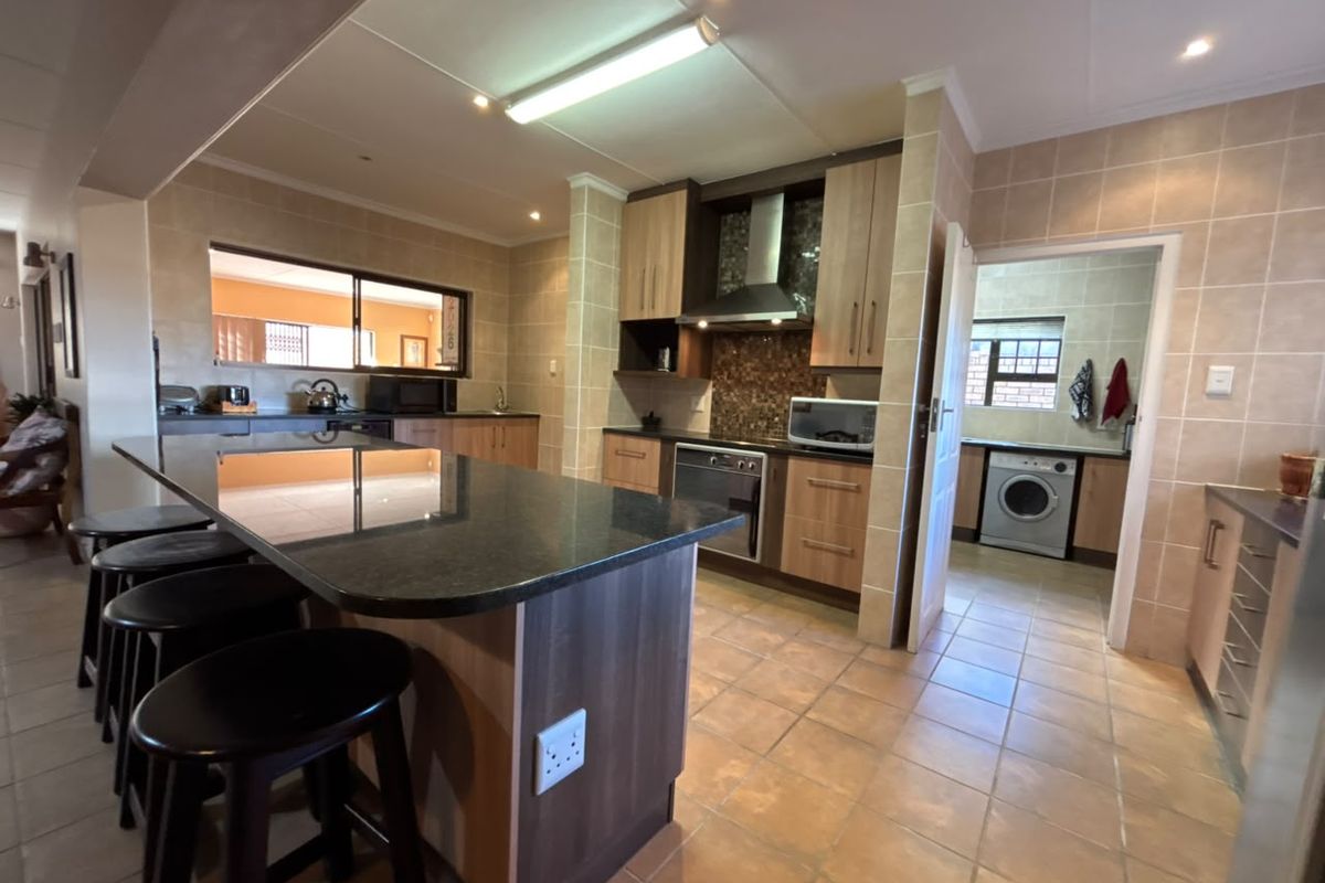 Spacious kitchen featuring a large granite island, fitted cabinetry, built-in oven, and an adjoining scullery area with laundry facilities.