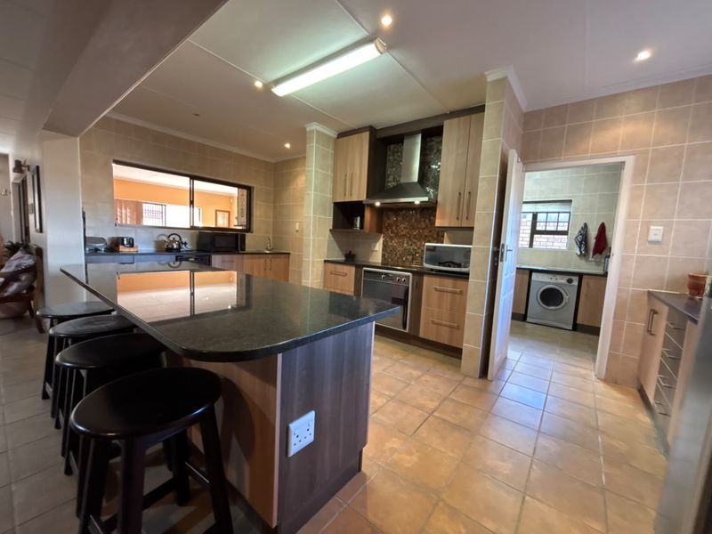 Spacious kitchen featuring a large granite island, fitted cabinetry, built-in oven, and an adjoining scullery area with laundry facilities.