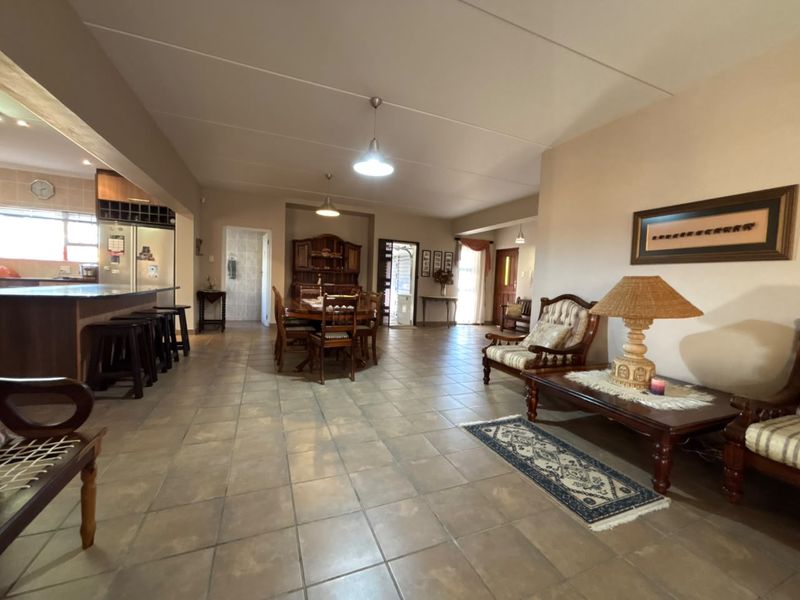 Spacious open-plan living and dining area featuring tiled flooring, a kitchen island with breakfast bar, and neutral wall finishes.