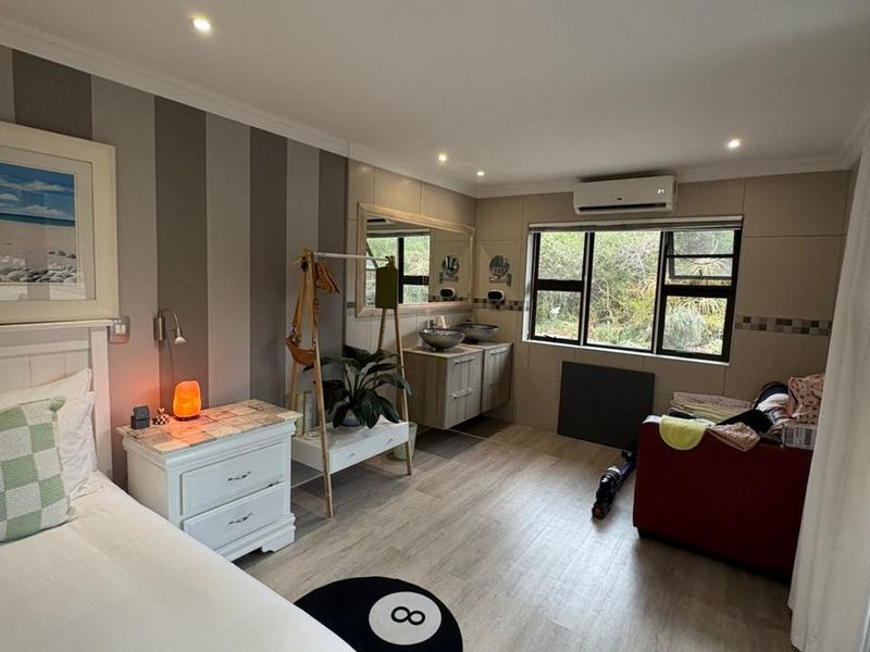 Spacious bedroom featuring an integrated vanity area with dual sinks, modern laminate flooring, and a wall-mounted air conditioning unit.