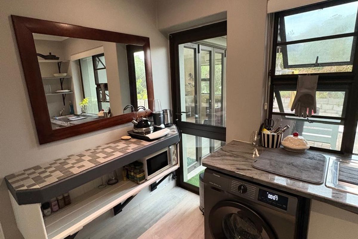 A functional laundry area featuring a stone countertop, stainless steel sink, built-in shelving, and direct access to the exterior through a glass door.