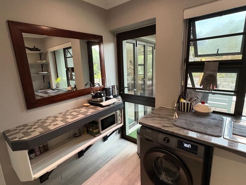 A functional laundry area featuring a stone countertop, stainless steel sink, built-in shelving, and direct access to the exterior through a glass door.