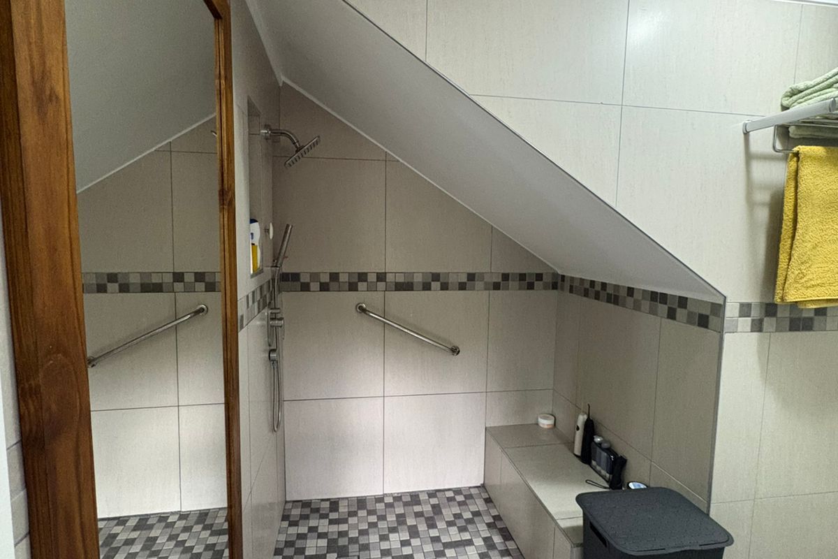 A modern bathroom featuring a walk-in shower with a built-in bench, grab rails, and neutral wall tiling with a decorative mosaic border.