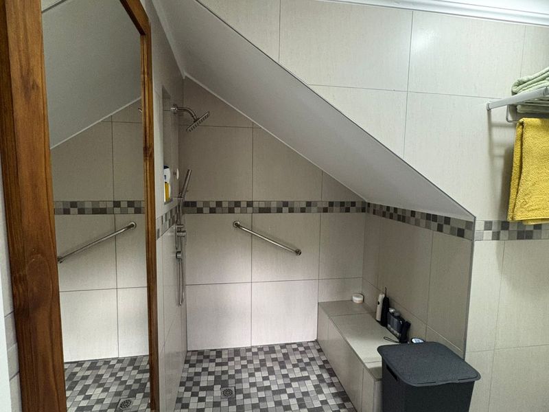 A modern bathroom featuring a walk-in shower with a built-in bench, grab rails, and neutral wall tiling with a decorative mosaic border.