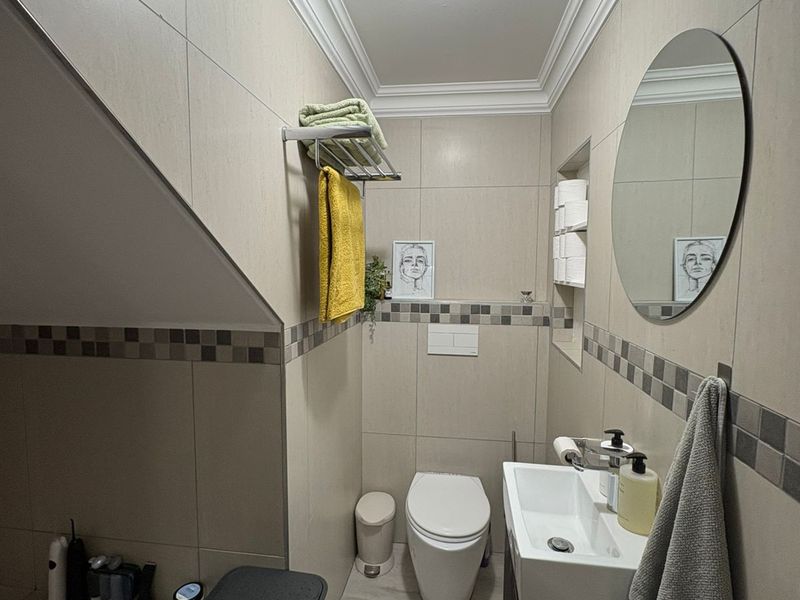 A compact, modern bathroom featuring a wall-mounted toilet, vanity basin, and neutral tiled finishes with decorative mosaic accents.
