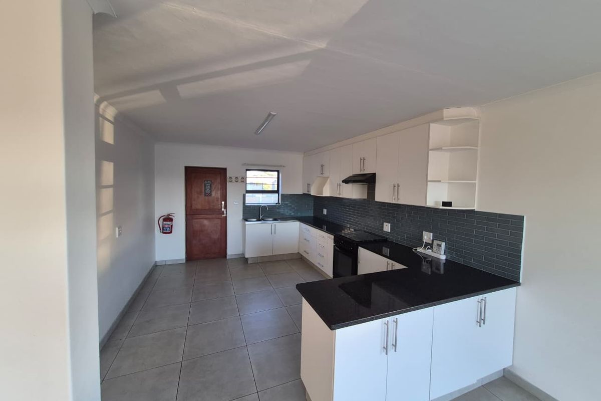 A clean, modern kitchen featuring white cabinetry, contrasting black granite countertops, dark subway tile backsplash, and tiled flooring in an open-plan layout.