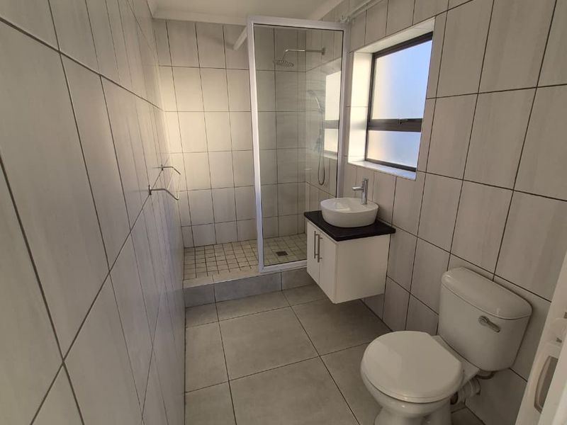 A clean, modern bathroom featuring a walk-in shower, wall-mounted vanity with a vessel sink, and neutral floor-to-ceiling tiling.