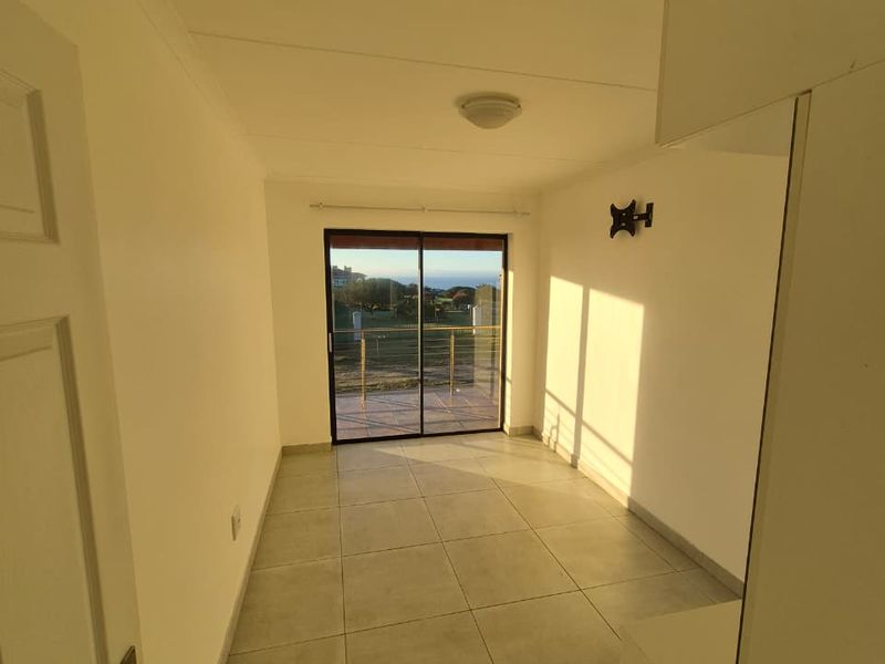 An empty bedroom featuring neutral tiled flooring, a built-in cupboard, and a sliding glass door providing access to an outdoor area.