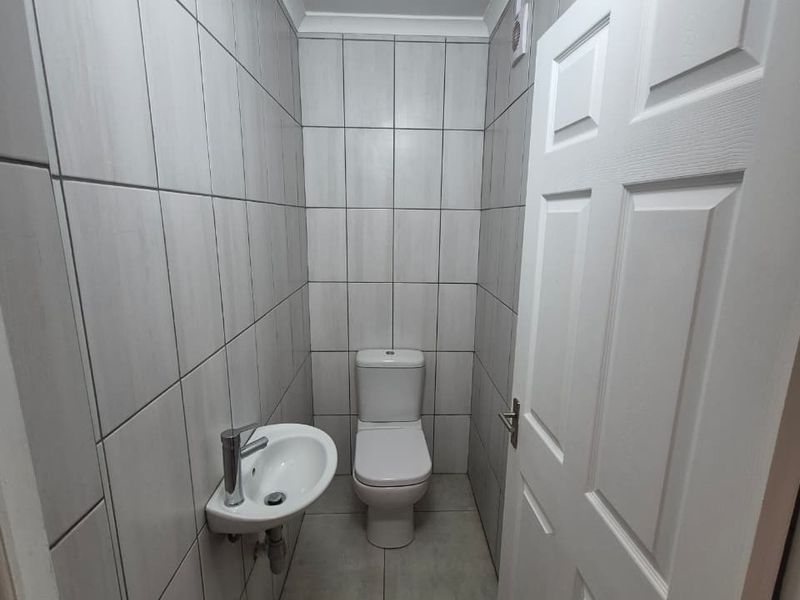 A compact, modern guest bathroom featuring neutral ceramic wall and floor tiles, a wall-mounted basin, and a standard toilet.