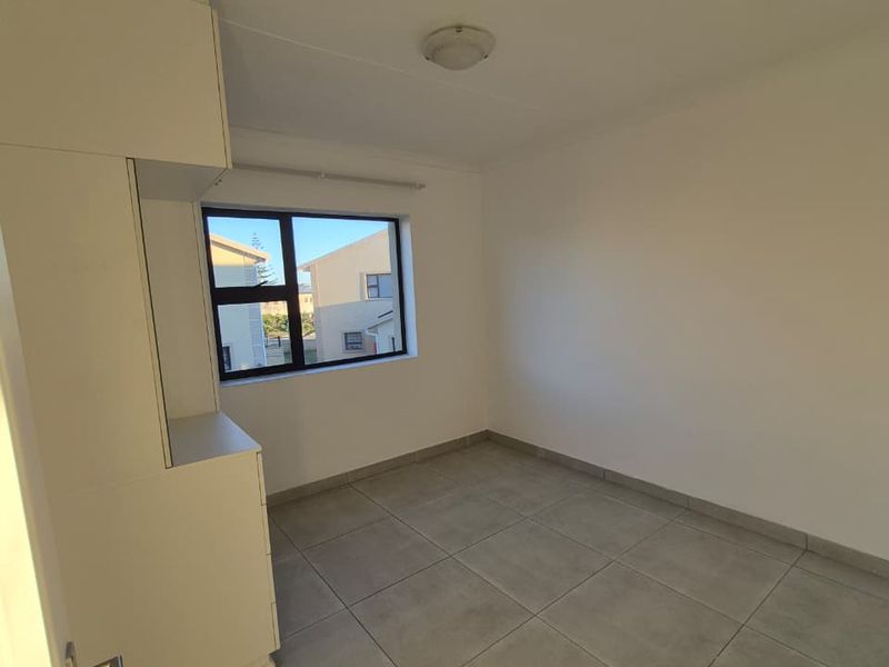 A clean, empty bedroom featuring neutral tiled flooring, built-in cupboards, and an aluminium-framed window providing natural light.