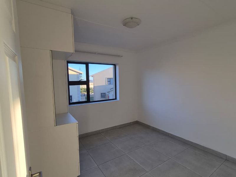 A clean, empty bedroom featuring neutral tiled flooring and built-in storage cupboards, offering a blank canvas for personalization.
