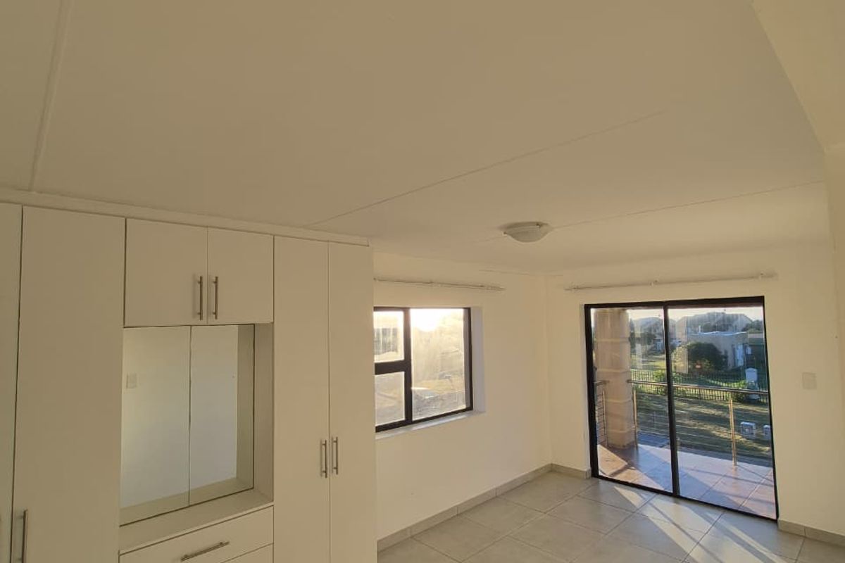 Bright and spacious bedroom featuring neutral tiled flooring, extensive built-in cabinetry with integrated mirror, and direct access to a private balcony.