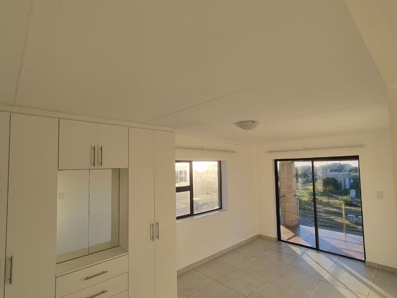 Bright and spacious bedroom featuring neutral tiled flooring, extensive built-in cabinetry with integrated mirror, and direct access to a private balcony.