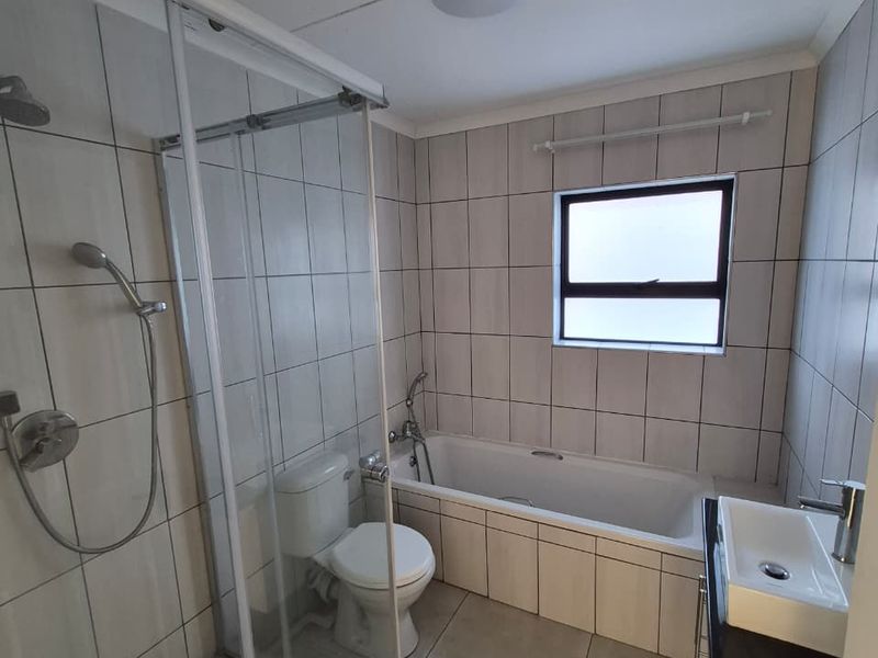 A functional bathroom featuring a glass shower enclosure, a built-in bathtub, a vanity cabinet, and neutral ceramic tiling throughout.
