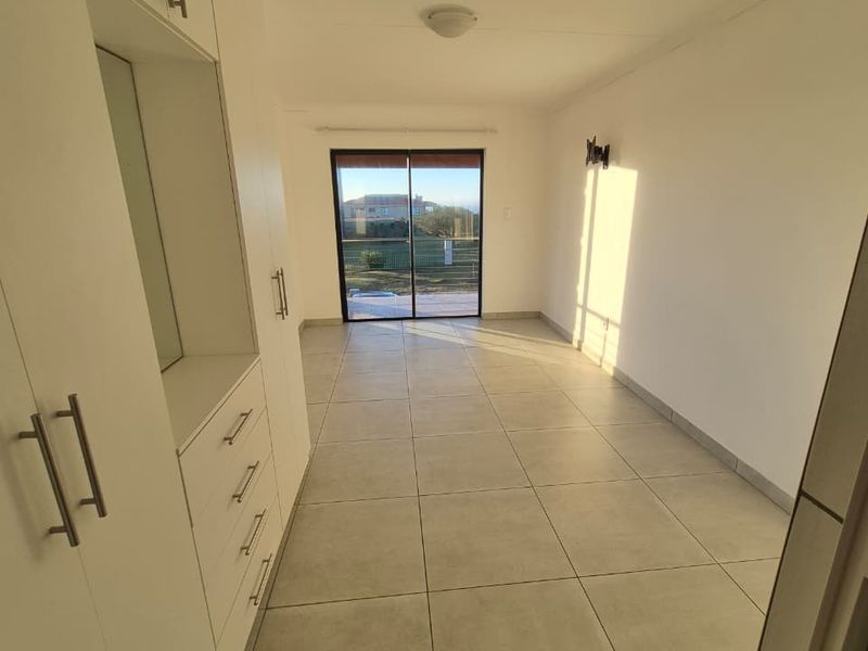 A bright, empty bedroom featuring neutral tiled flooring, ample built-in cupboard storage, and a sliding glass door providing access to the exterior.