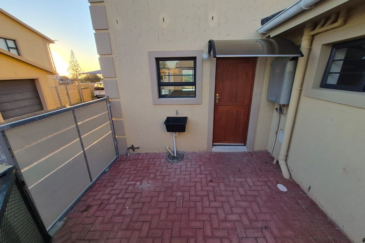 A paved rear courtyard area featuring an external utility sink, a timber door with a protective awning, and an exterior electrical distribution board.