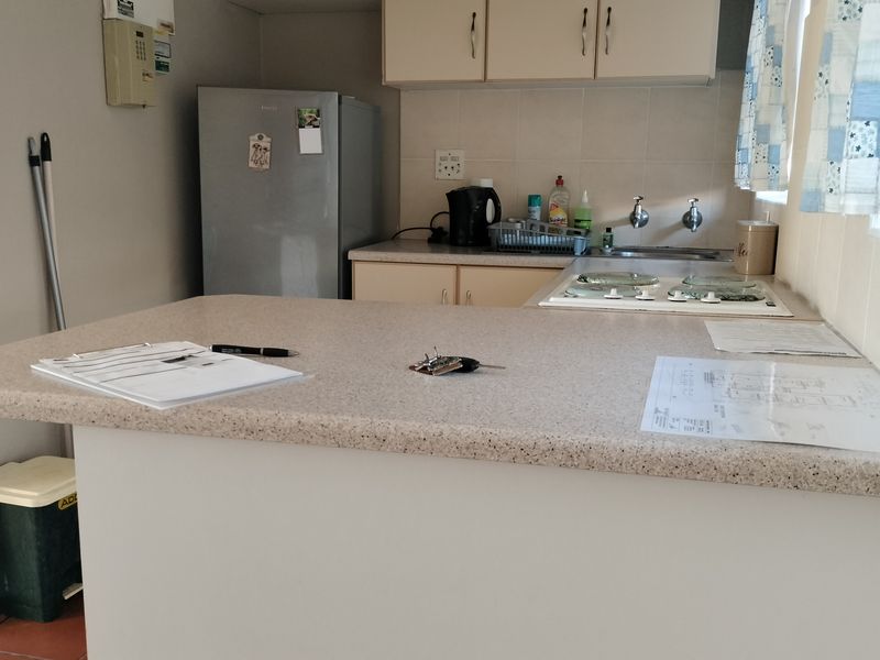 A functional kitchen featuring laminate countertops, built-in cabinetry, a hob, and a tiled backsplash, offering a practical layout for daily meal preparation.