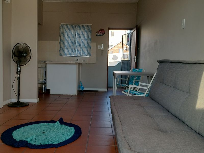 Open-plan living area featuring tiled flooring and a compact kitchen counter, providing a functional layout with direct access to an exterior space.