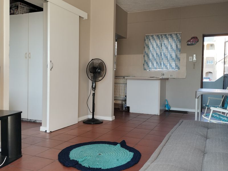 Open plan living area featuring tiled flooring and a compact kitchen space with built-in cabinetry and direct access to an exterior entrance.