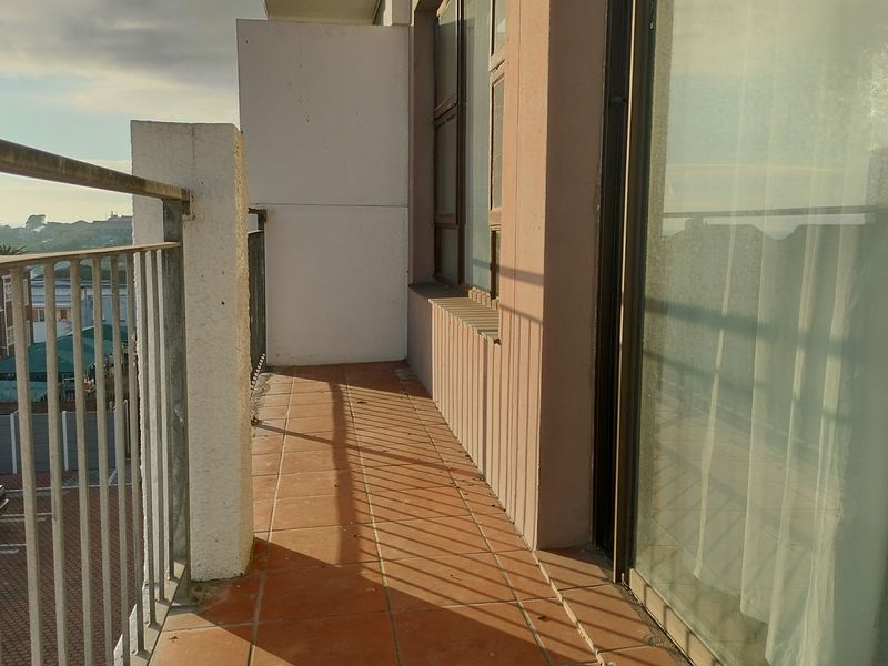 A functional balcony area featuring tiled flooring and a metal balustrade, accessible via a large sliding glass door.