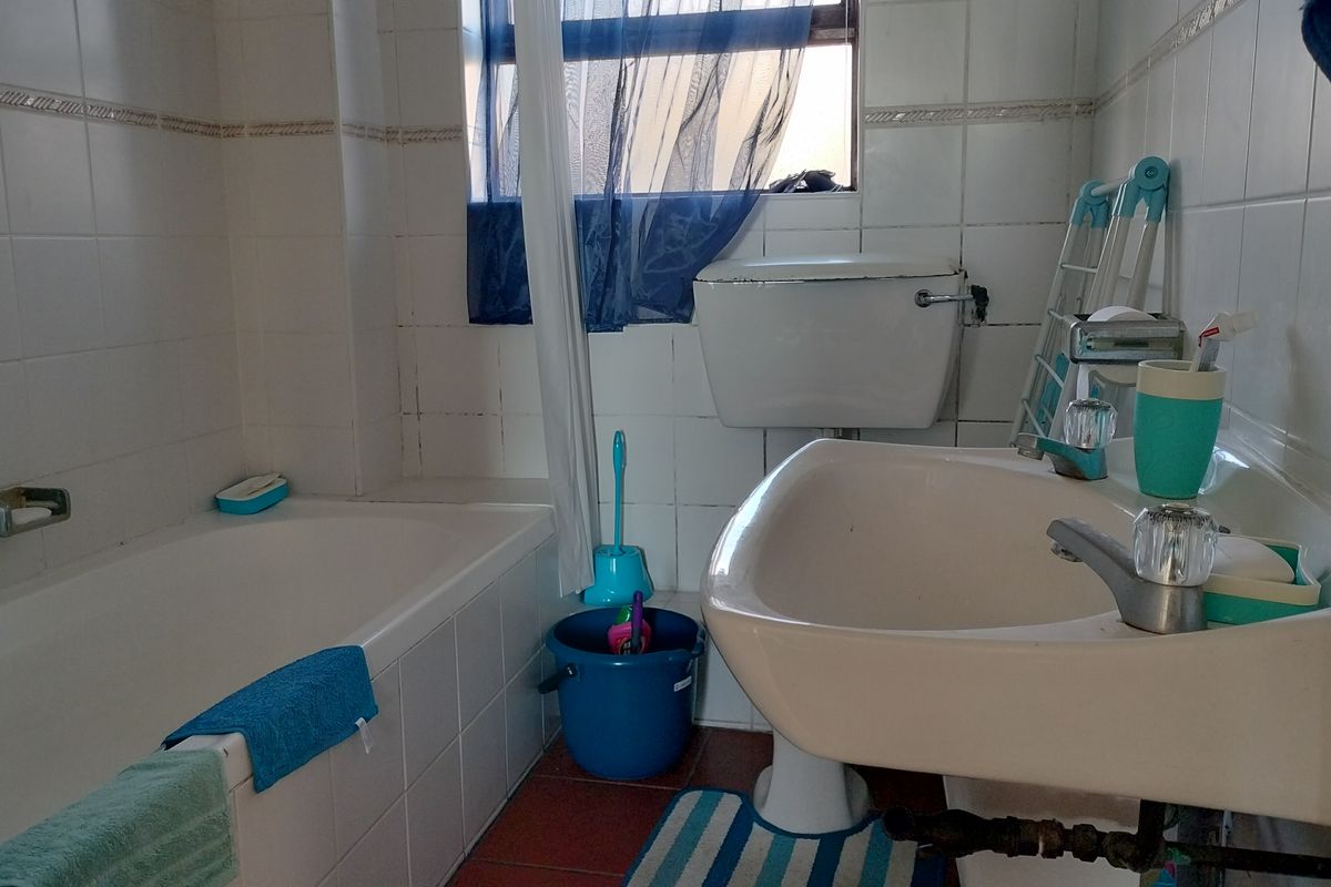 A functional bathroom featuring a bathtub, pedestal basin, and toilet, with tiled finishes throughout. The space would benefit from modern updates to fixtures and finishes.