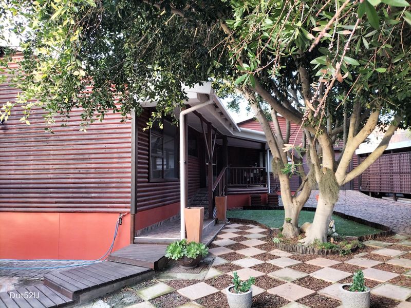 Rear exterior view of a log cabin style home featuring a paved patio area, timber decking, and mature landscaping.