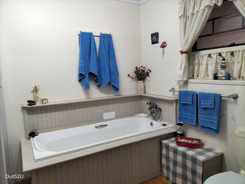 A functional bathroom featuring a built-in bathtub with beadboard paneling, a towel rail, and a window with security bars.