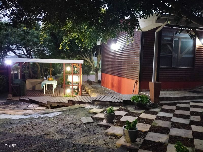 Rear exterior view featuring timber decking, timber-clad wall, and a checkered paved garden path under mature trees.