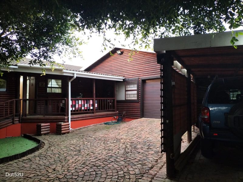 Front view of a log cabin style house featuring a brick paved driveway, covered carport, and a timber veranda entrance.