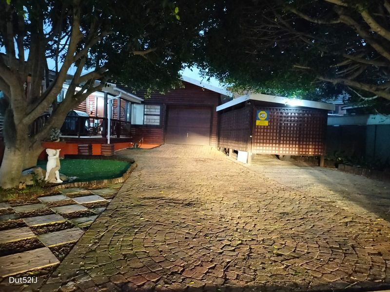 Front exterior view of a timber-clad house featuring a cobblestone driveway, attached garage, and a covered carport area at night.