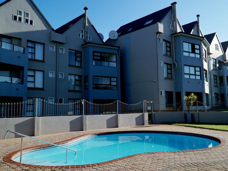 A well-maintained communal swimming pool area featuring a paved deck, metal fencing, and a clear view of the multi-story apartment building facade.