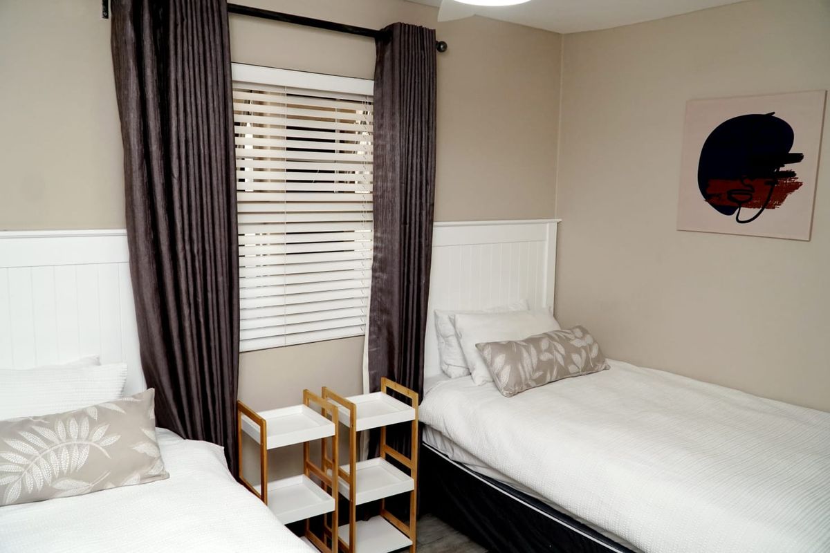 A well-maintained bedroom featuring neutral wall tones, venetian blinds, and a curtain rod, providing a clean and functional living space.