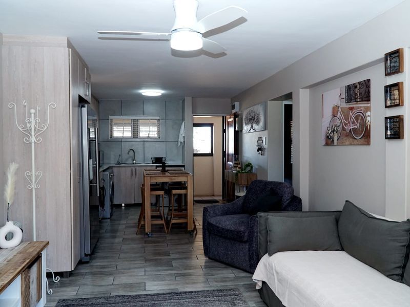 An open-plan living and kitchen area featuring modern tiled flooring, neutral cabinetry, and a ceiling fan, creating a functional and cohesive living space.