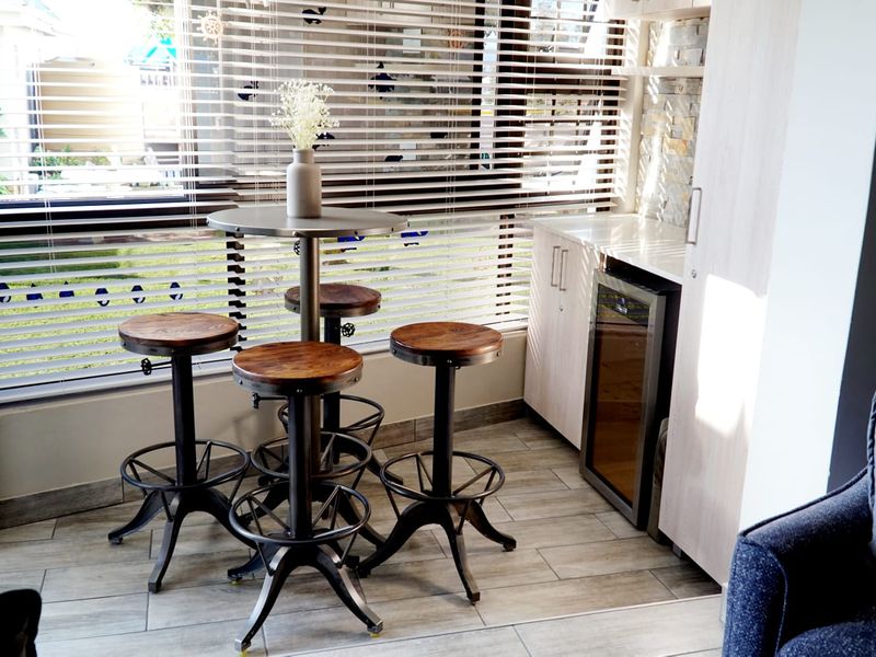 A modern bar area featuring built-in cabinetry, an integrated wine cooler, stone veneer wall accents, and large windows with venetian blinds.