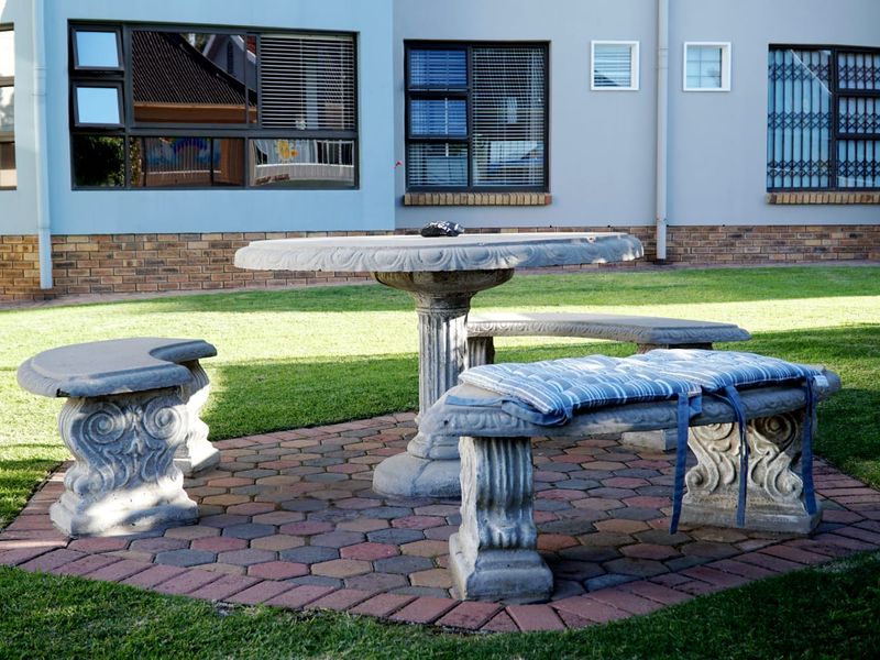 A well-maintained rear garden area featuring a paved patio space with stone seating and views of the apartment building's exterior facade.