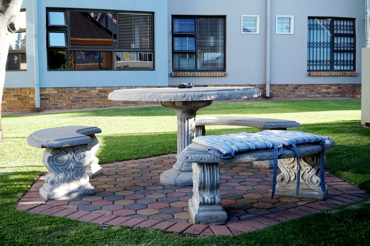 A well-maintained rear garden area featuring a paved patio space with stone seating and views of the apartment building's exterior facade.