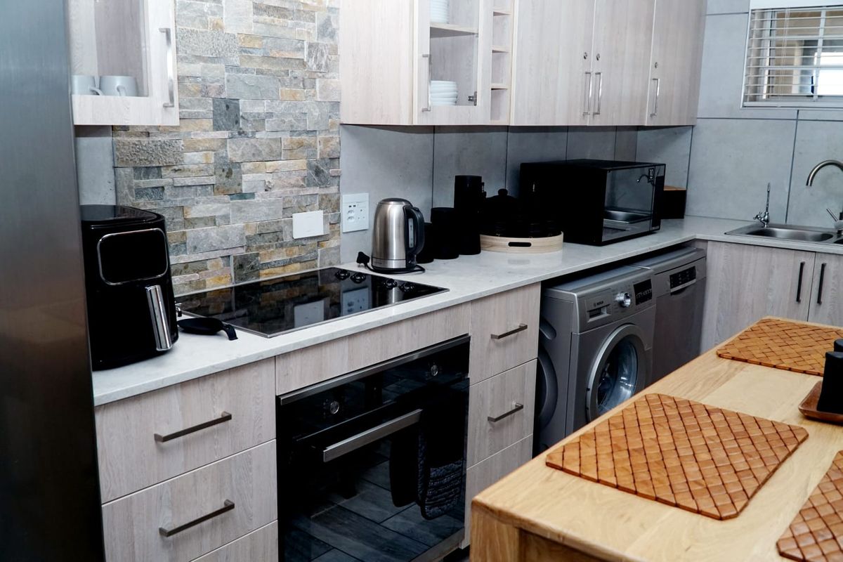 Modern kitchen featuring light wood cabinetry, stone-look tile backsplash, integrated appliances, and a sleek electric hob with built-in oven.