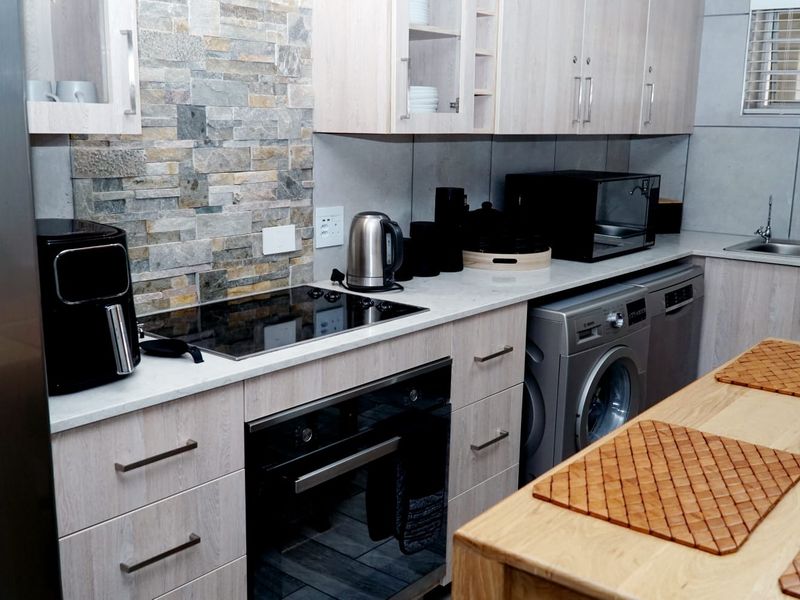 Modern kitchen featuring light wood cabinetry, stone-look tile backsplash, integrated appliances, and a sleek electric hob with built-in oven.