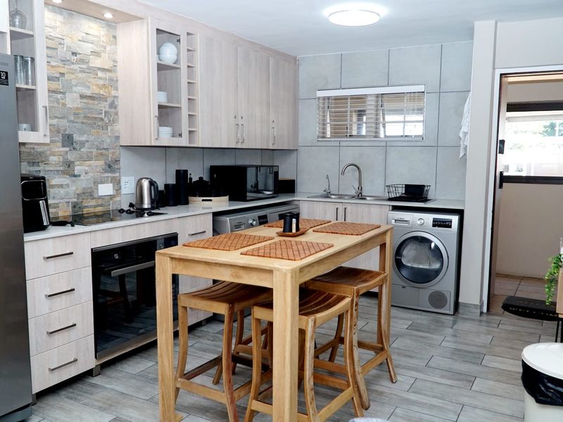 Modern kitchen featuring light wood cabinetry, stone veneer backsplash, integrated oven, electric hob, and double sink with tiled flooring and wall finishes.