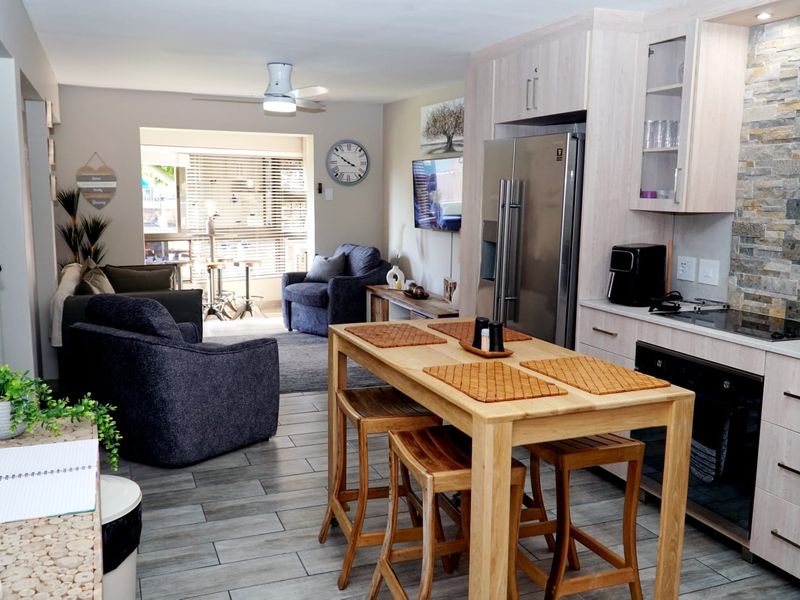 Open-plan living and kitchen area featuring modern cabinetry, stone tile backsplash, tiled flooring, and a ceiling fan, creating a cohesive and functional living space.