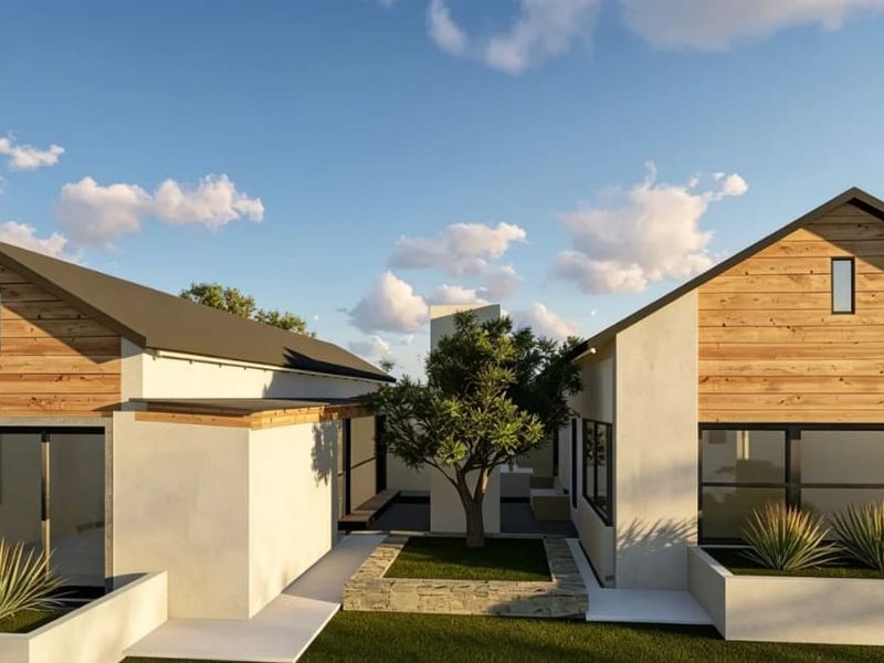 A modern architectural exterior view featuring dual structures with timber cladding, pitched roofs, and a central landscaped courtyard with a stone-clad planter.