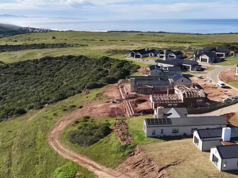 Aerial view of a coastal residential estate showing completed homes and ongoing construction projects with scenic ocean and landscape views.