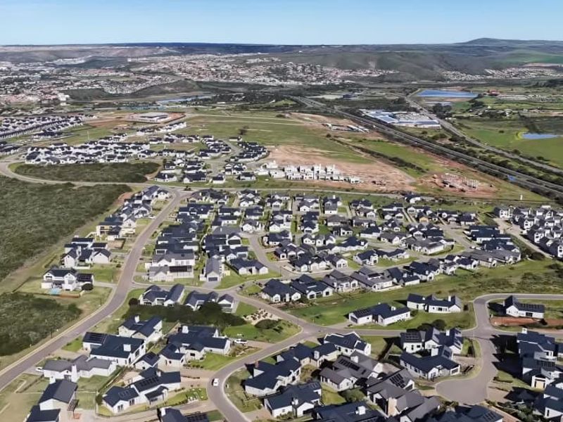 An aerial view of a modern residential estate featuring numerous detached homes, paved road networks, and surrounding natural landscape.