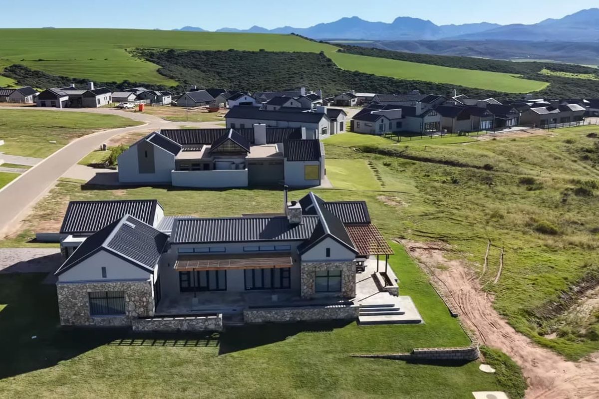 Aerial view of a modern residential property featuring stone cladding, metal roofing, and a landscaped garden within a scenic estate setting.