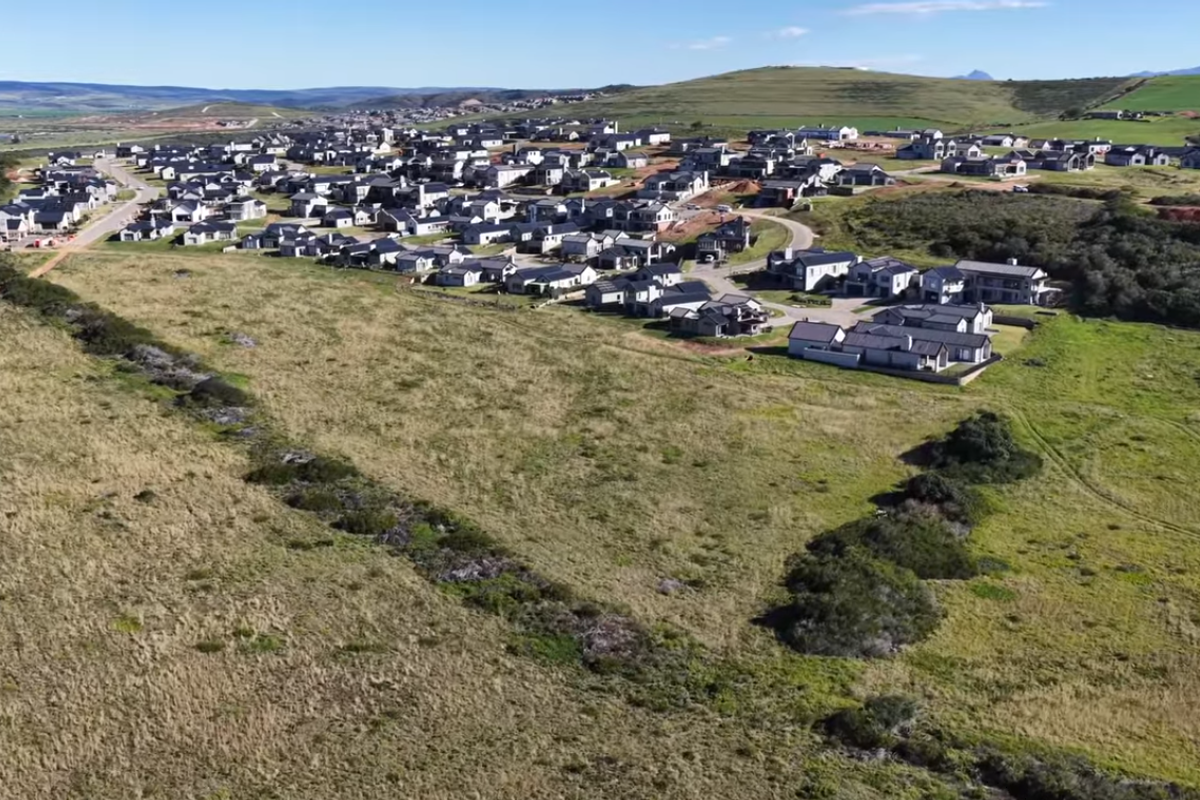 An aerial view of a modern residential estate development set within a natural landscape, showcasing the layout of homes and surrounding infrastructure.