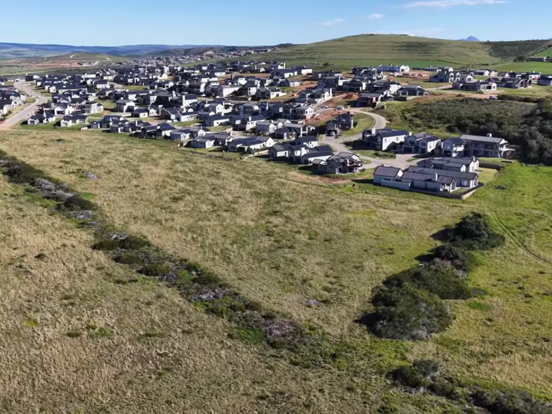 An aerial view of a modern residential estate development set within a natural landscape, showcasing the layout of homes and surrounding infrastructure.