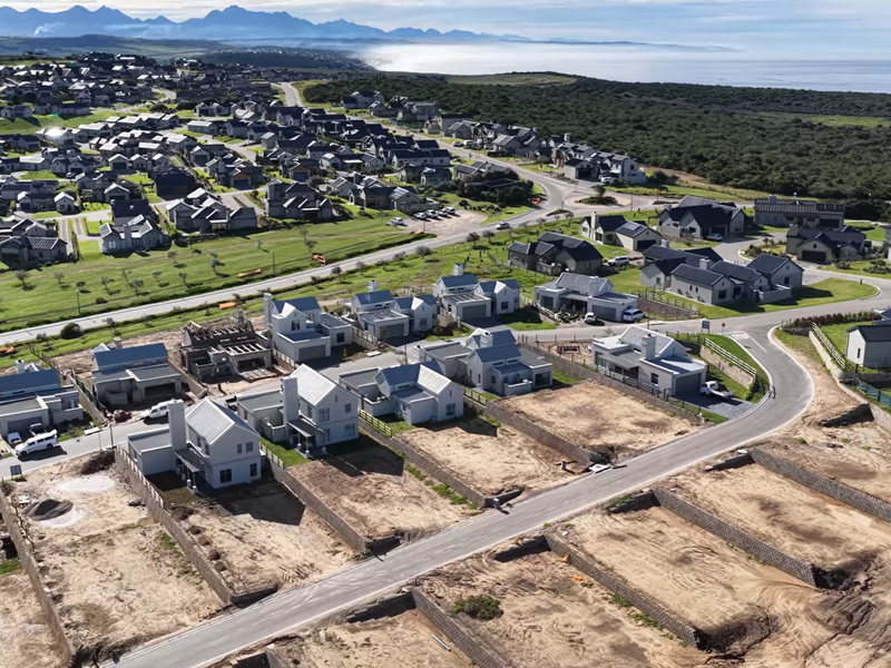 Aerial view of a modern residential estate development featuring paved roads, retaining walls, and scenic coastal surroundings.